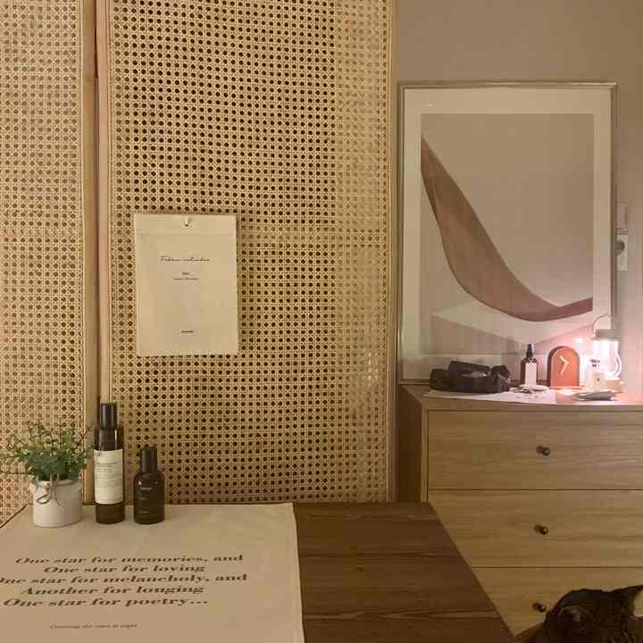 Beige and natural toned bedroom featuring rattan partition, wooden dresser, table clock, and plant creating a cozy atmosphere