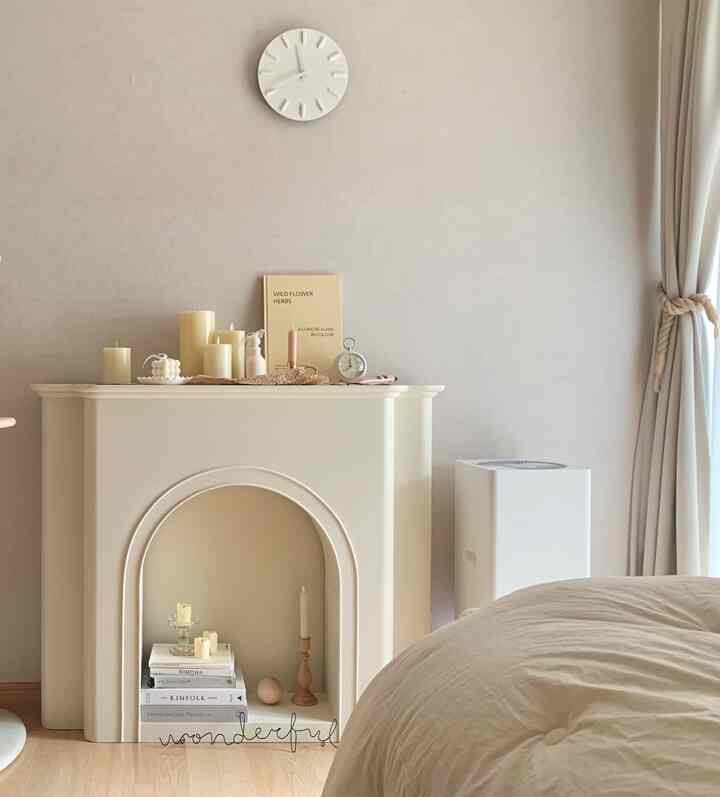 ベージュとホワイトの調和が取れた寝室、暖炉とキャンドル、時計が配置された雰囲気のあるインテリア