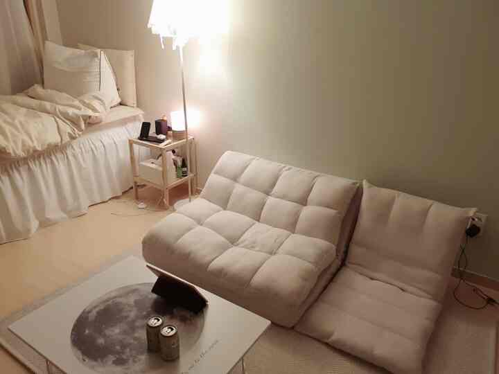 ベージュとアイボリーのトーンの9坪ワンルーム、シンプルなソファとベッド、フロアランプが温かみのある雰囲気を演出する空間