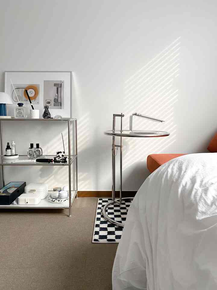 Bright and clean bedroom in white and brown tones, featuring an orange sofa and a metal side table