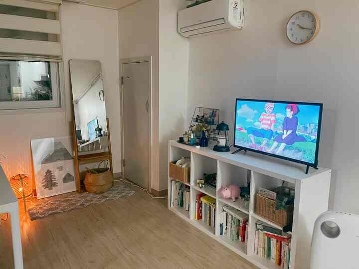 White walls and wood tone floor in living room featuring white bookshelf with TV and clock, creating a natural modern style space