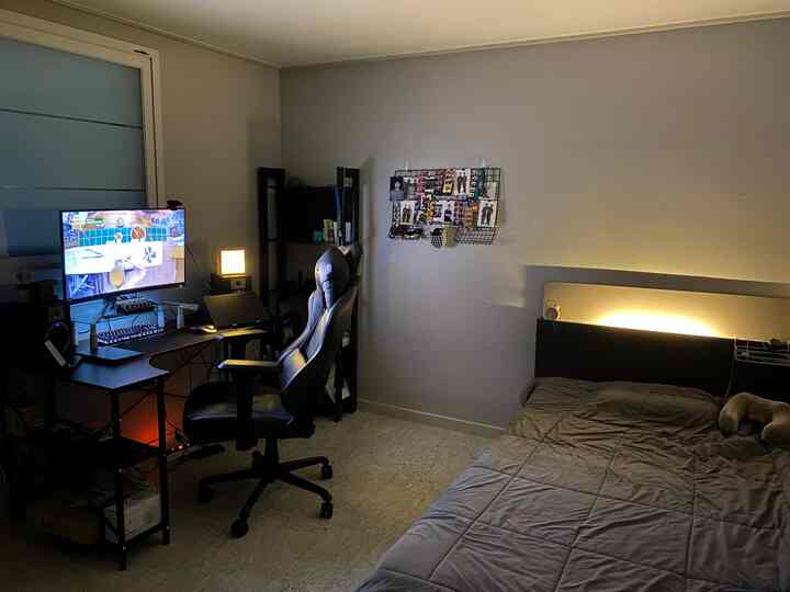 ブラックとグレーのトーンの一人暮らし寝室、ゲーミングデスクとパソコン、落ち着いたホームオフィスの照明がある雰囲気のあるインテリア