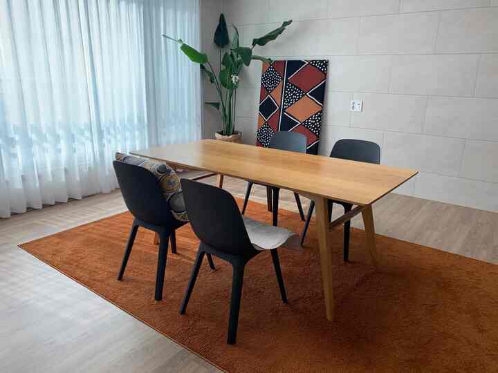 Natural color-toned, minimal style dining room for four, featuring warm orange rug, wooden table, and armchairs in a winter living room setting