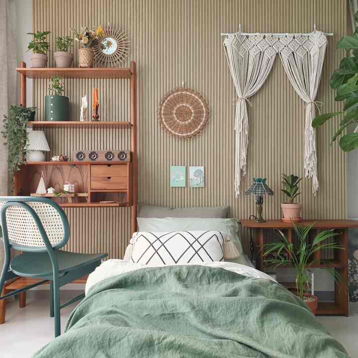 ベージュのナチュラルトーンの寝室、テンバボードの壁と木製家具、緑の寝具と植物が配置された雰囲気のある空間