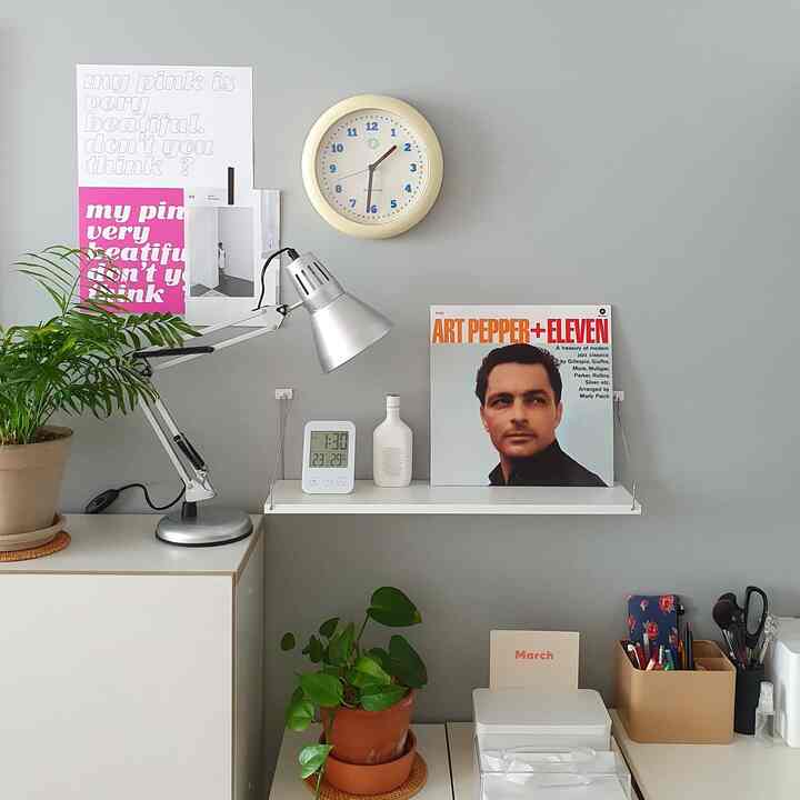 Gray-walled home office featuring a silver table lamp, poster, and clock creating a neat atmosphere