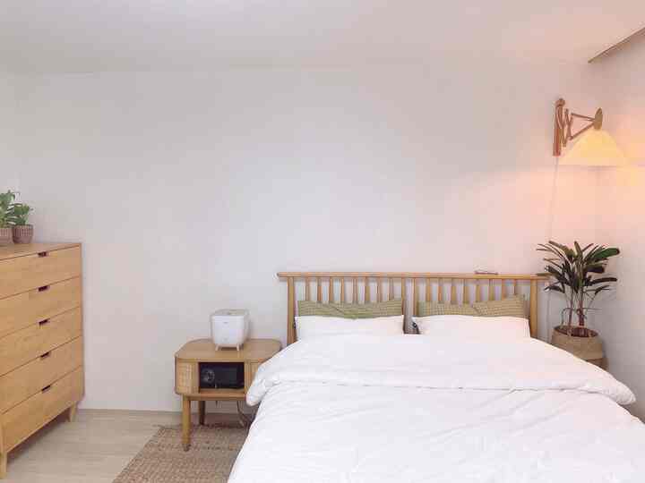 Wood tone and white bedroom featuring a bed, nightstand with hidden projector, and pleated wall lamp as accent lighting, creating a cozy relaxation space