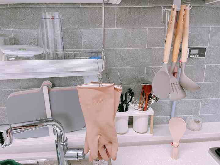 Kitchen space with gray tiled backsplash, wood-tone utensils, and beige rubber gloves hung above countertop