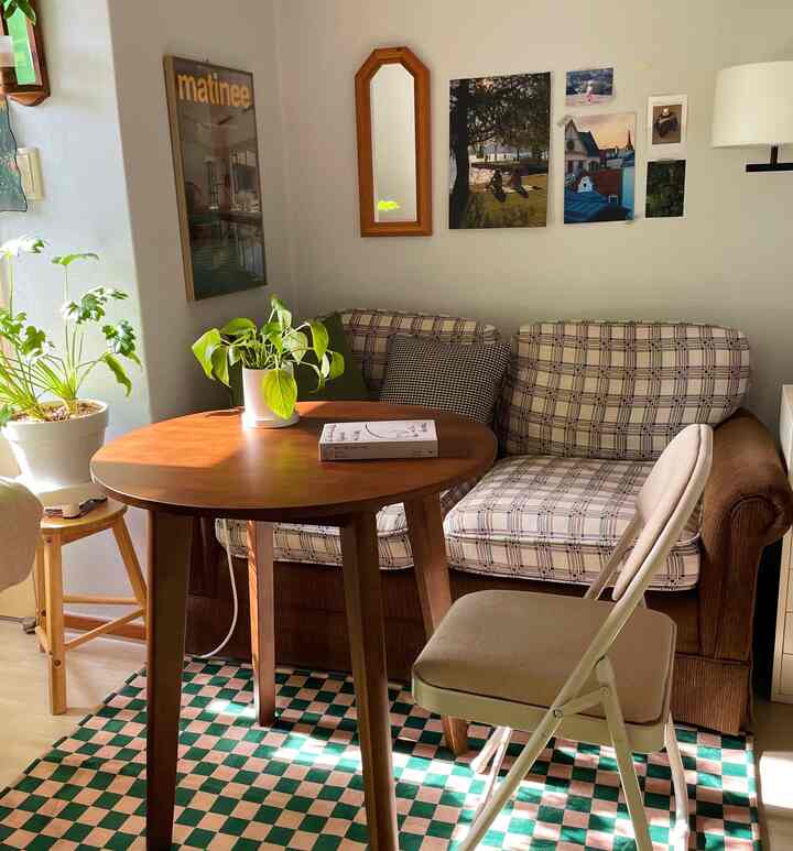 Warm wood tones and vintage patterned sofa in a studio home office space featuring a round table and checkered rug with cozy atmosphere