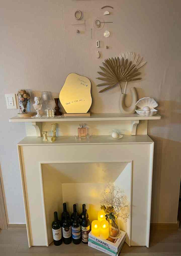 Beige and white toned living room fireplace space featuring vintage objets, LED candles, and dried flowers, creating a cozy and minimal interior