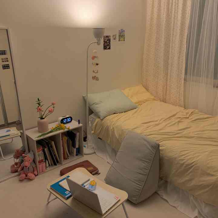 Beige-toned studio bedroom featuring yellow bedding and a compact home office with a simple and cozy atmosphere