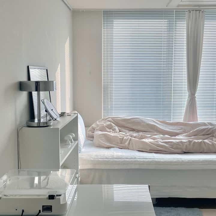 白とナチュラルカラーの寝室、整ったベッドとブラインドが配置されたシンプルで清潔感のあるインテリア