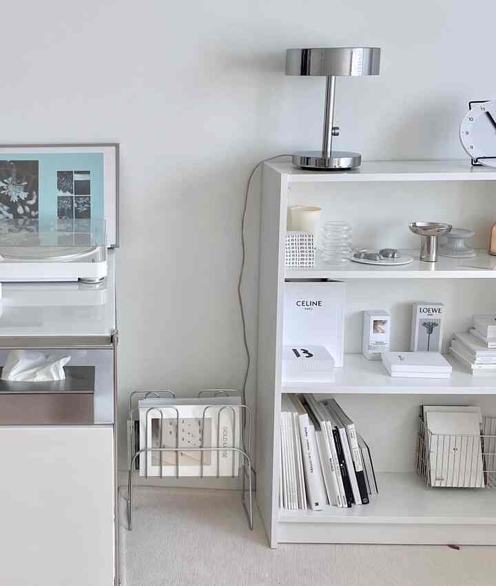 Modern study space with white and silver tones, featuring a neatly organized bookshelf and table lamp
