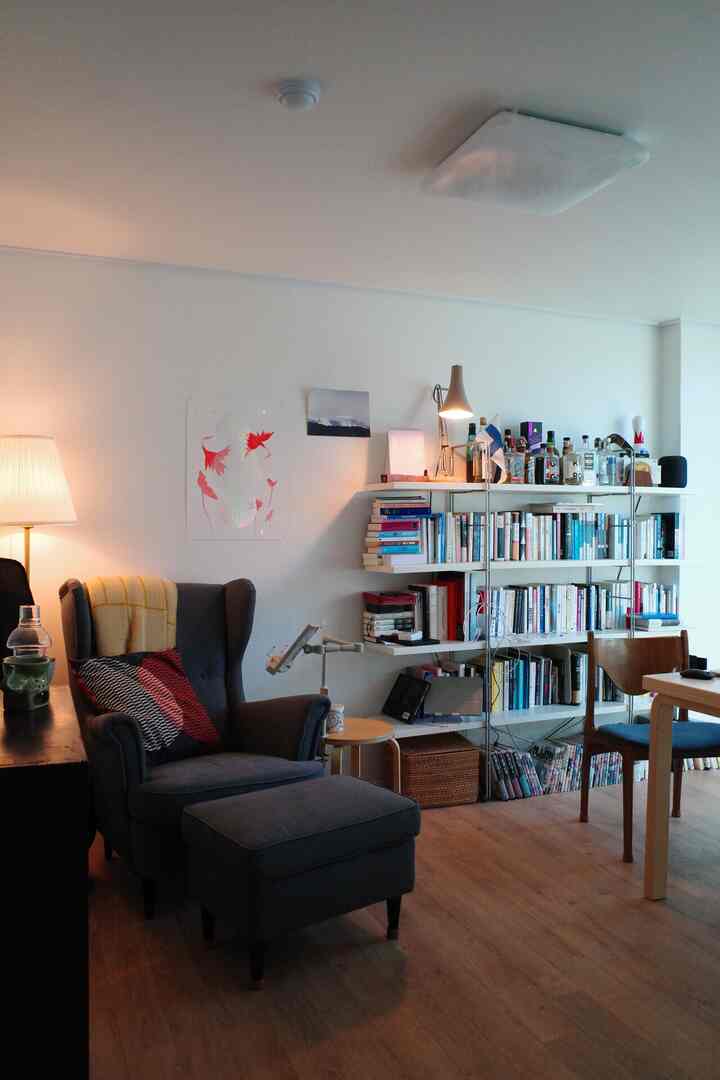 Natural-tone study space featuring a dark gray wing chair and white bookshelf, creating a cozy workspace