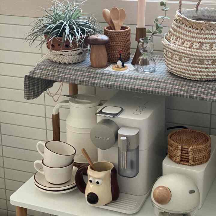 White and brown toned kitchen space featuring a coffee machine and stacked teacups creating a cozy home cafe atmosphere
