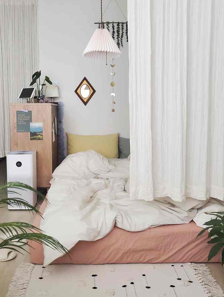 White and beige toned studio bedroom featuring a simple bed and plants creating a cozy atmosphere