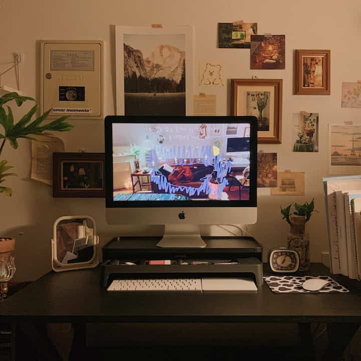 ブラウンの木製額縁と植物が配置された黒いデスクにiMacモニターがある温かみのあるホームオフィス空間