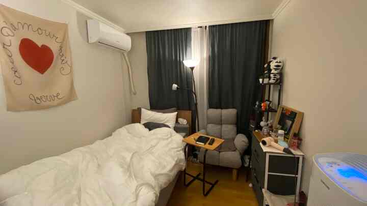 Cozy small bedroom with white bed and black curtains, featuring a gray armchair and dresser