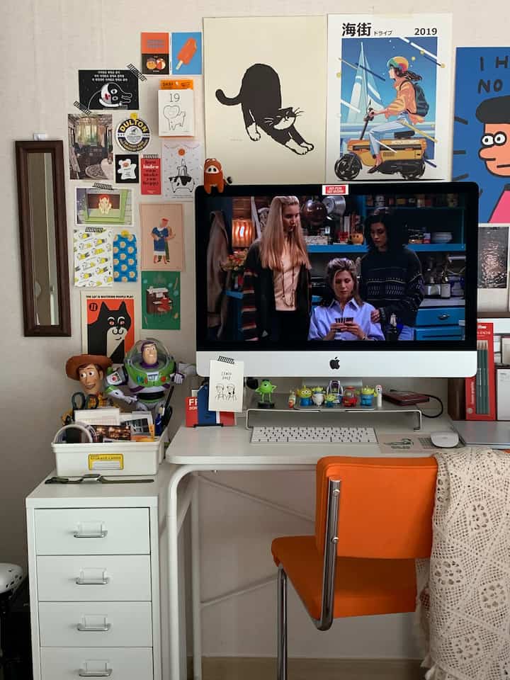 White-walled home office workspace featuring a desk and orange chair with eclectic wall art