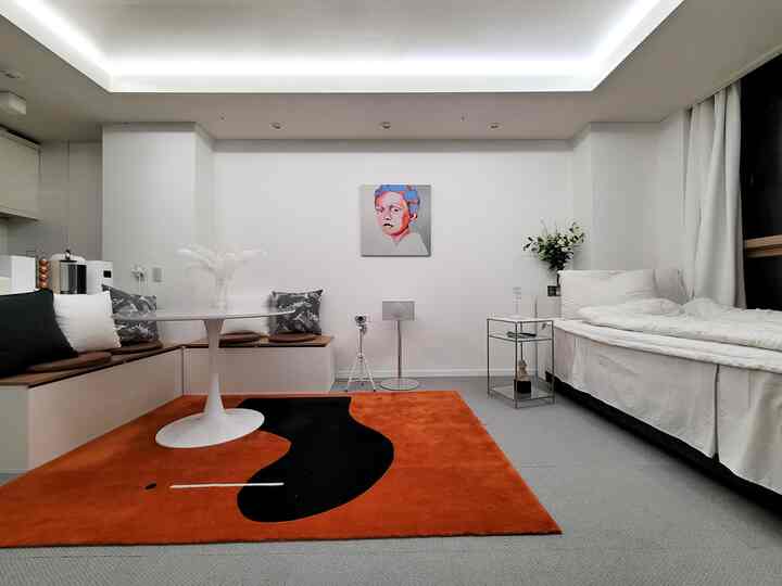 Modern living room with white and orange tones featuring a round table, bench seating, and a sofa bed on the right side