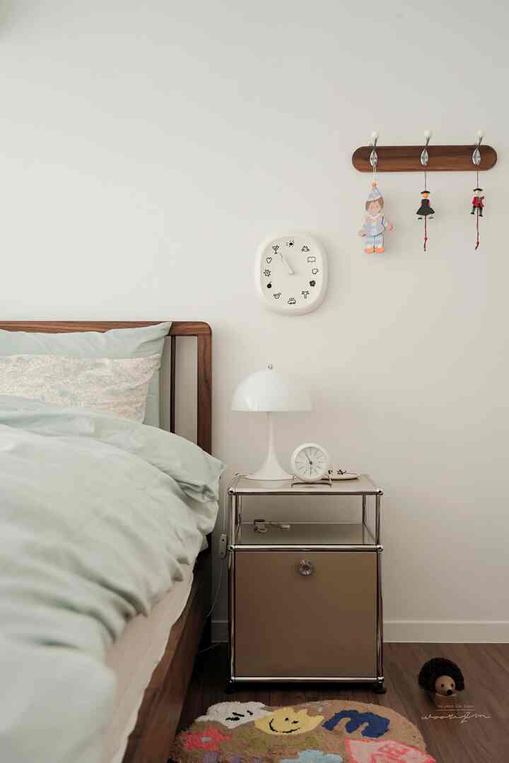 Cozy bedroom with white walls, wood-tone bed frame, sky blue bedding, and a nightstand with a lamp