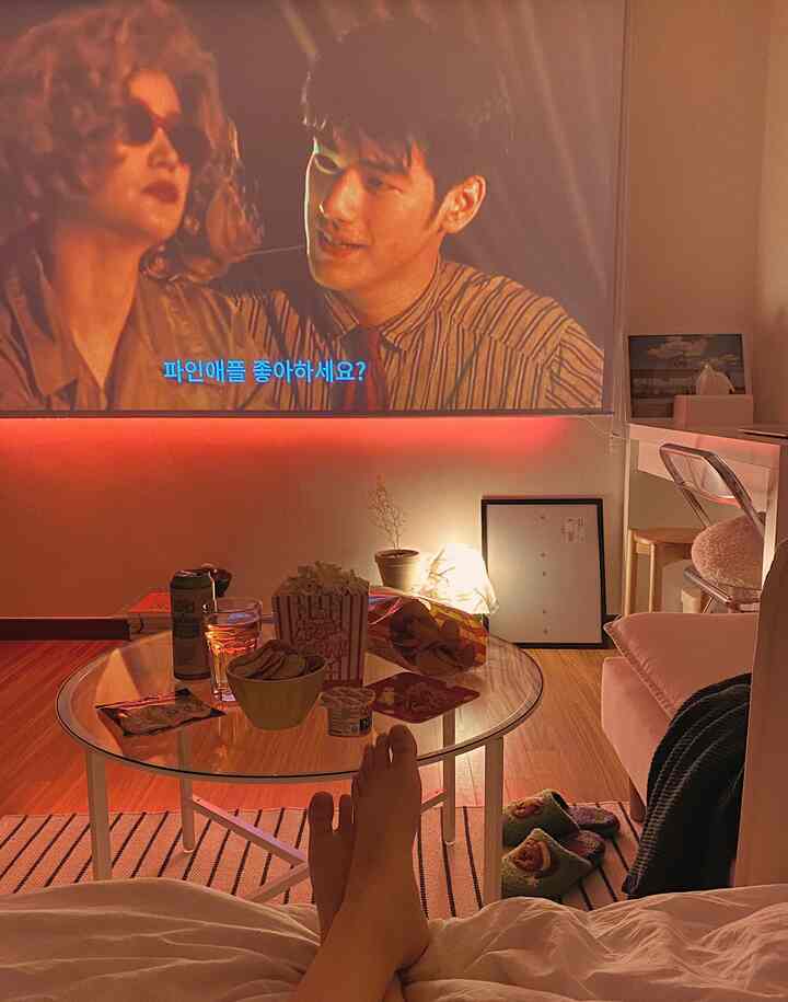 A cozy, modern living room with white and wood tones featuring a projector screen and coffee table in a home cinema setup