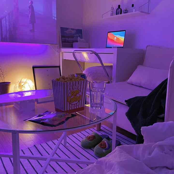 Purple-lit living room with white sofa, round coffee table, and a neat home office setup featuring a laptop