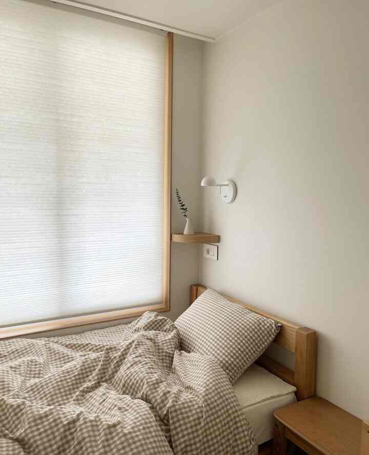 Beige and wood tone minimal bedroom featuring gingham bedding and a wall sconce, creating a cozy atmosphere