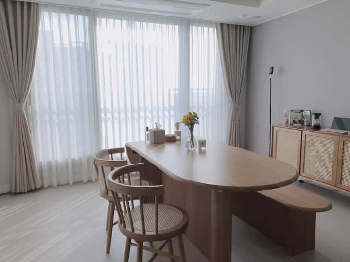 Bright, natural wood-tone dining table and chairs with beige curtains in a spacious living room