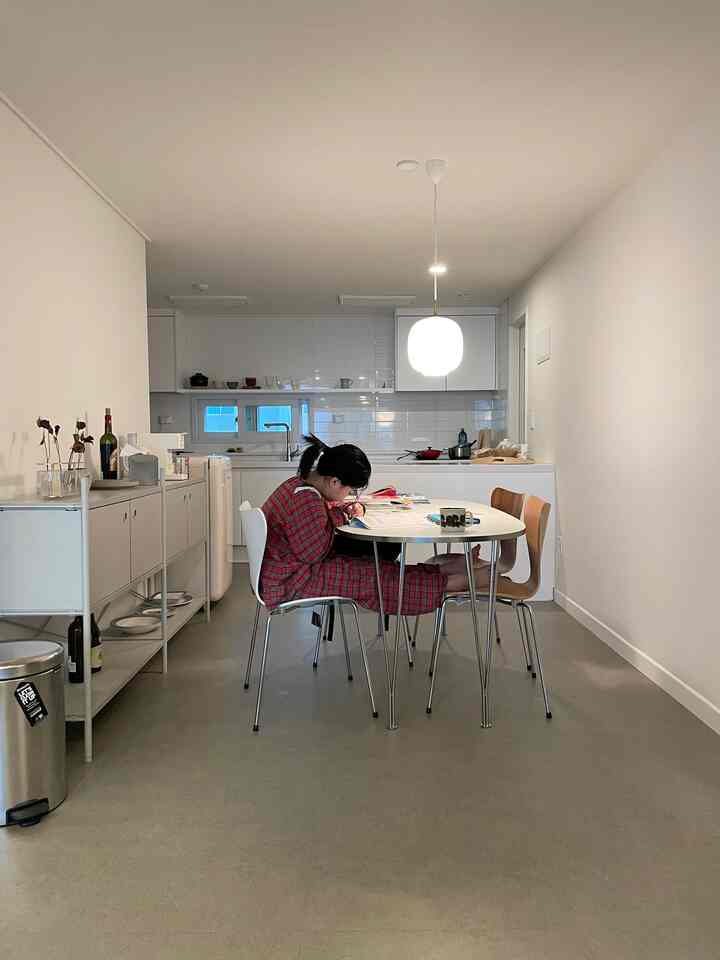 白とグレーのトーンが調和したキッチンとダイニングルーム、シンプルモダンな空間にてテーブルで読書する人が温かみを演出