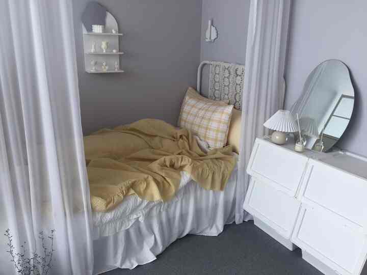 Cozy bedroom with gray walls and white curtains featuring a super single bed with yellow duvet and checkered pillow, white dresser embodying natural modern style