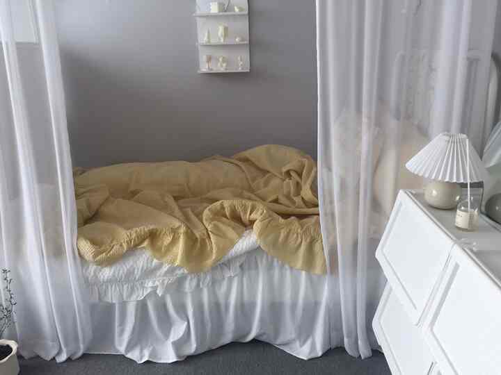 Cozy bedroom featuring soft yellow bedding, white bedspread, and sheer white curtains creating a bright atmosphere