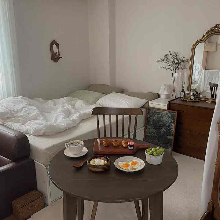 白と茶色のトーンでまとめられたワンルーム寝室とダイニング、木製テーブルと椅子、そしてホームブランチがある雰囲気の良いインテリア