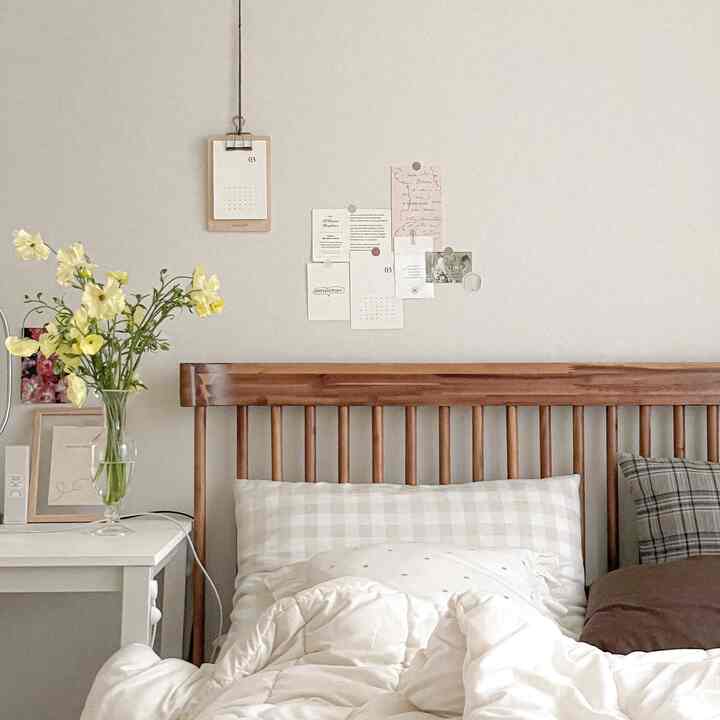 Natural-toned bedroom featuring wooden bed, white bedding, and a white bedside table with yellow flowers, creating a cozy atmosphere