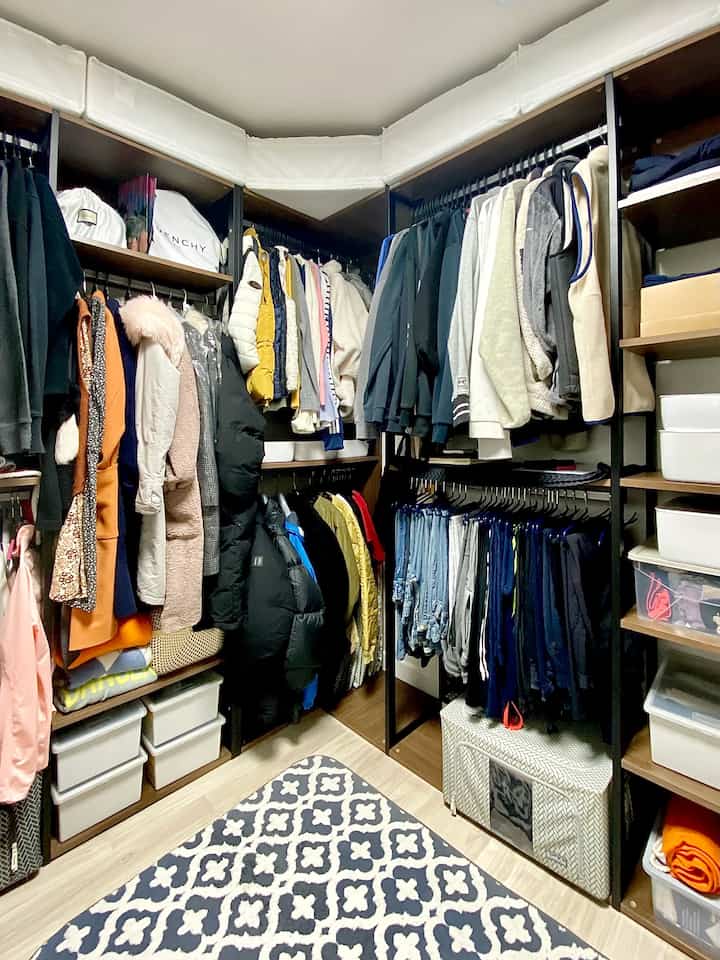 Natural tones and white storage boxes blend in a compact walk-in closet with diverse clothes and organized storage solutions