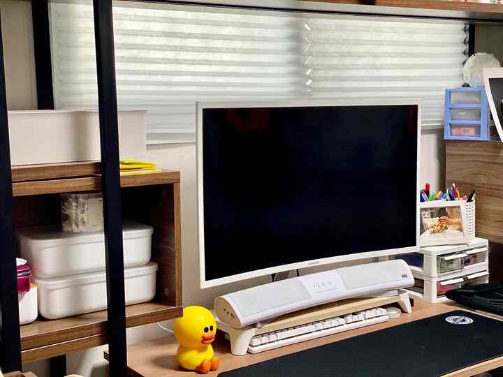 White-toned walk-in closet and study featuring a large monitor and storage boxes, creating a clean and functional workspace