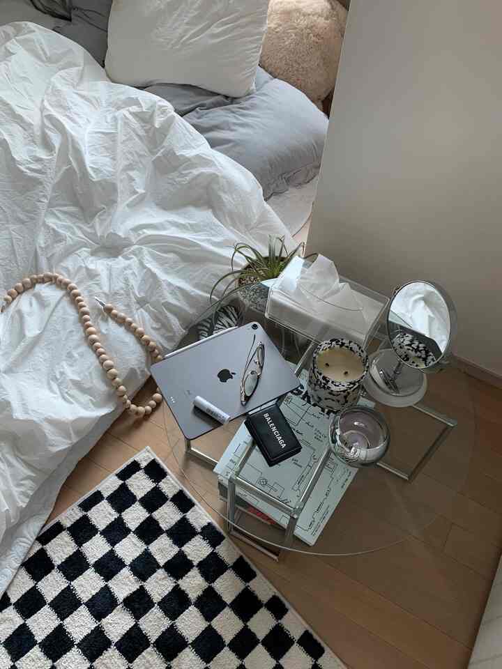 白とグレーのトーンのモダンな寝室、透明な丸いコーヒーテーブルとチェッカーパターンのラグが配置された雰囲気のあるインテリア