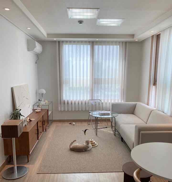 ナチュラルな色調のリビング、ベージュのラグの上で遊ぶ猫とシンプルなソファ、丸いサイドテーブルが配置された落ち着いた空間