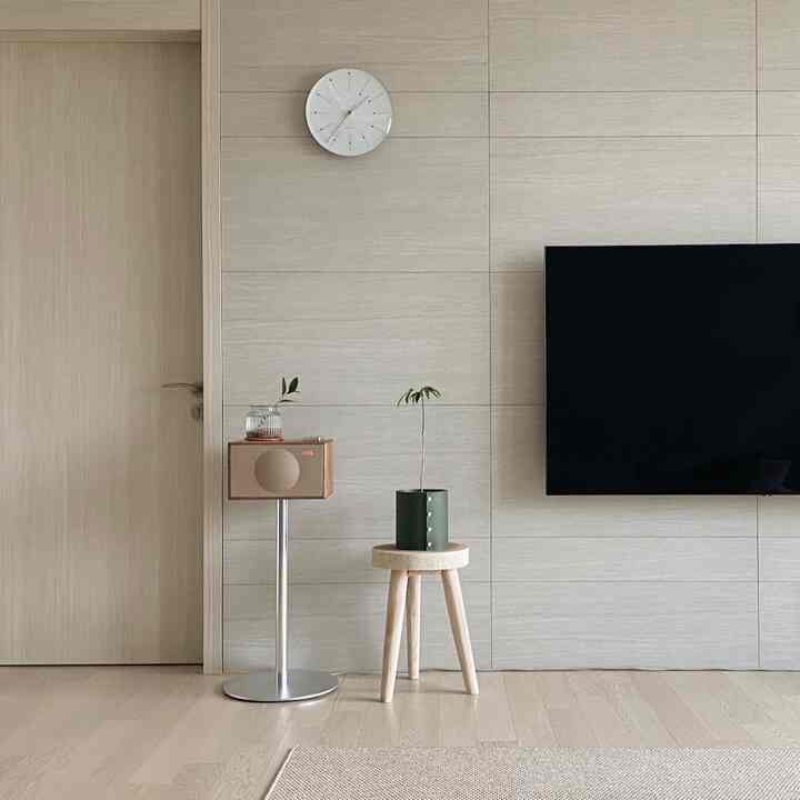 Natural beige-toned living room featuring a Geneva speaker, wooden stool with a small plant, and a simple modern interior