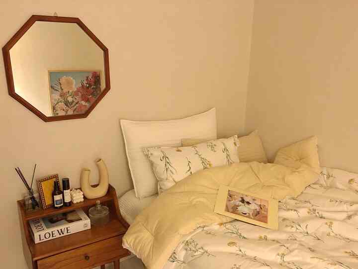 Yellow and white toned bedroom featuring a wooden side table and an octagonal wall mirror creating a cozy atmosphere
