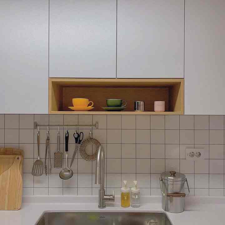 White and wood tone kitchen space featuring neatly arranged utensils and coffee cups with a clean, practical style