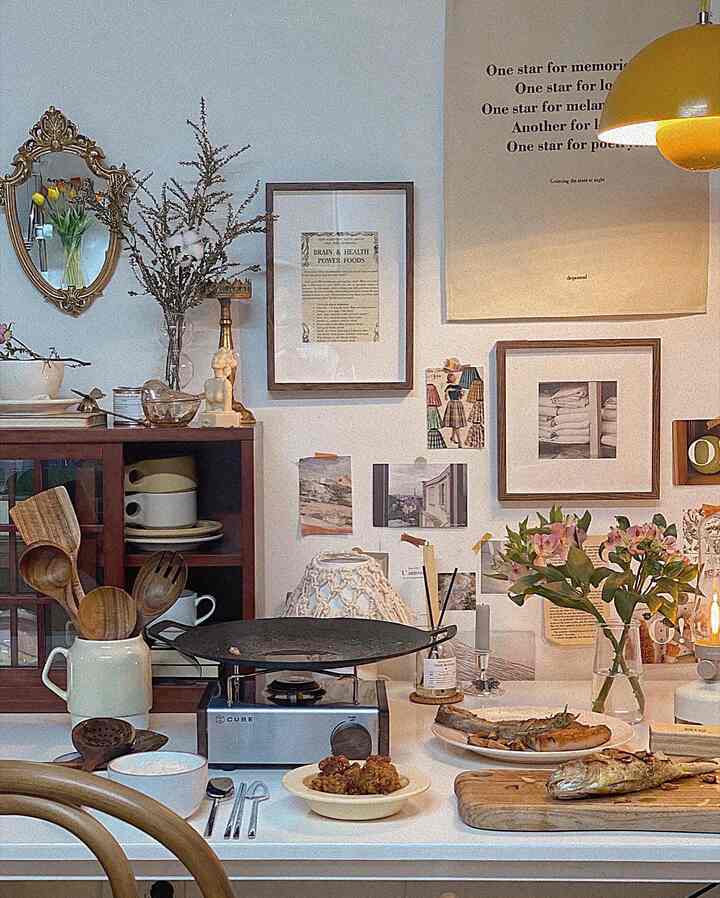 淡いブルーの壁と木目調家具が調和するキッチン、ヴィンテージの額縁や調理器具が配置された雰囲気のあるインテリア