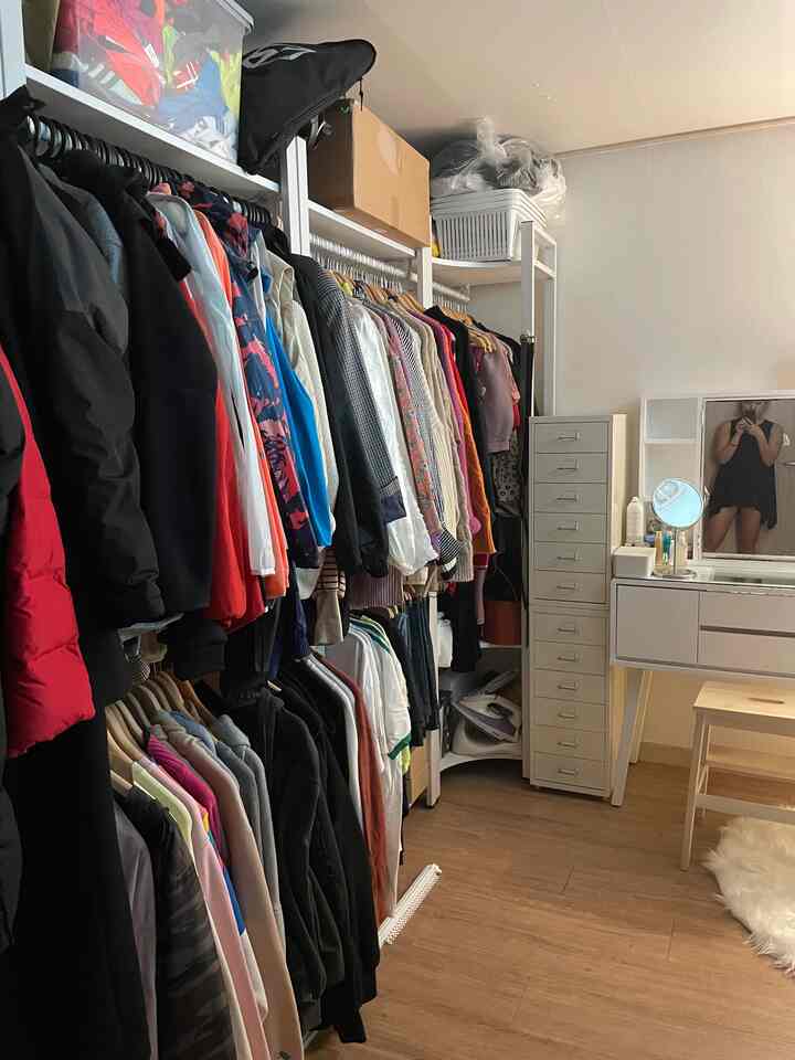 ナチュラルな色調のコンパクトなウォークインクローゼット、左側に洋服掛け、右側に化粧台が配置された整った空間