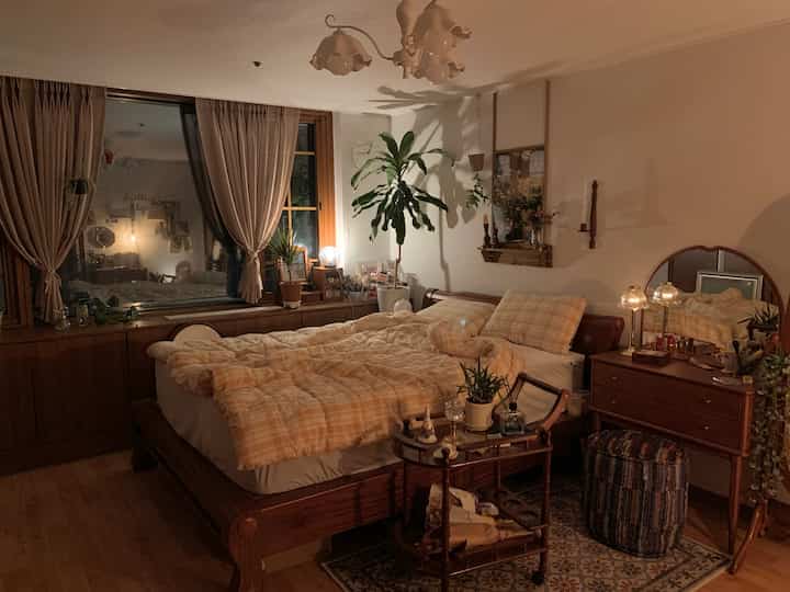 A cozy bedroom with soft beige and wood tones featuring a bed with yellow check bedding and a vintage vanity dresser