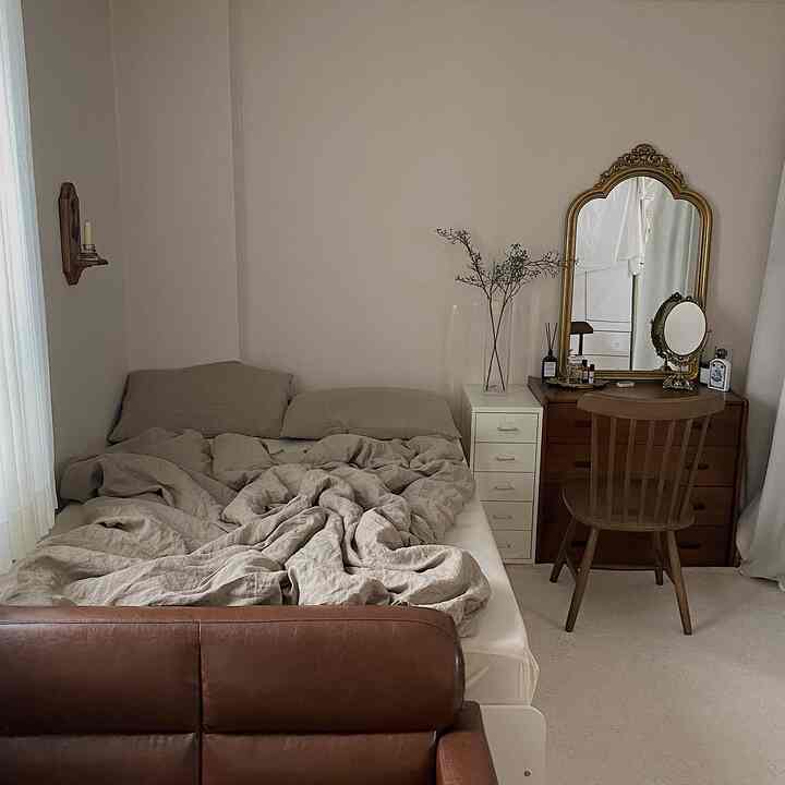 ベージュと木目調が調和した寝室、ヴィンテージ風アンティークミラーと木製家具が配置されたシンプルでナチュラルなインテリア