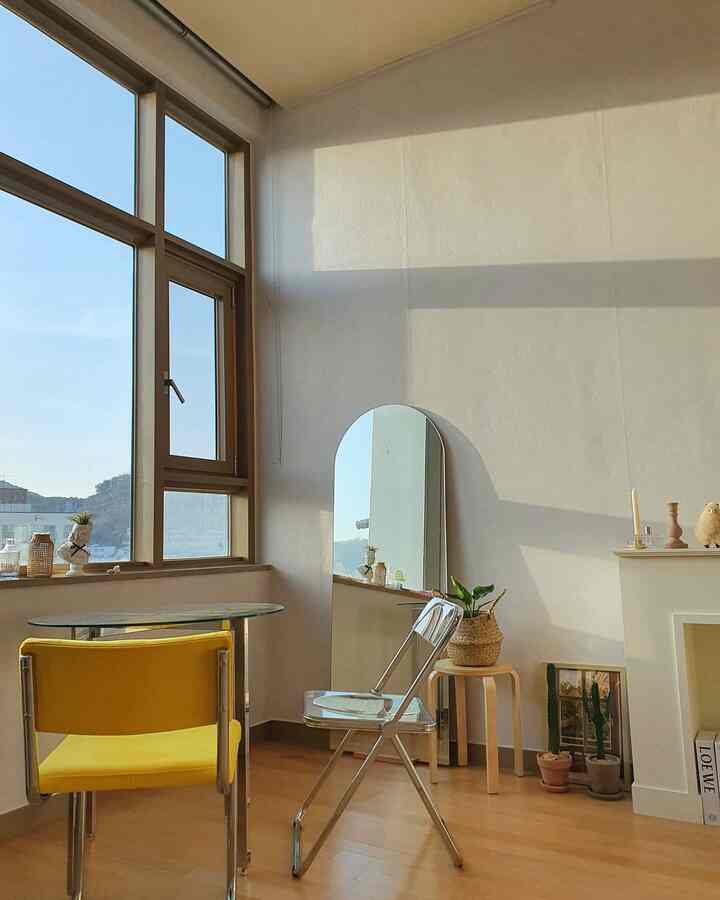 明るい黄色の椅子と木目調の床、大きな窓とアーチ型の全身鏡がある白いワンルーム空間