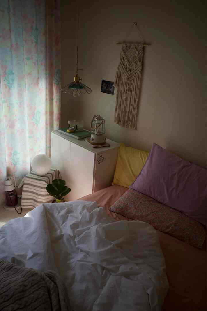 柔らかなベージュ色の壁とパステル調の寝具が調和した寝室、花柄のカーテンと可愛らしい小物が配置された温かみのあるインテリア