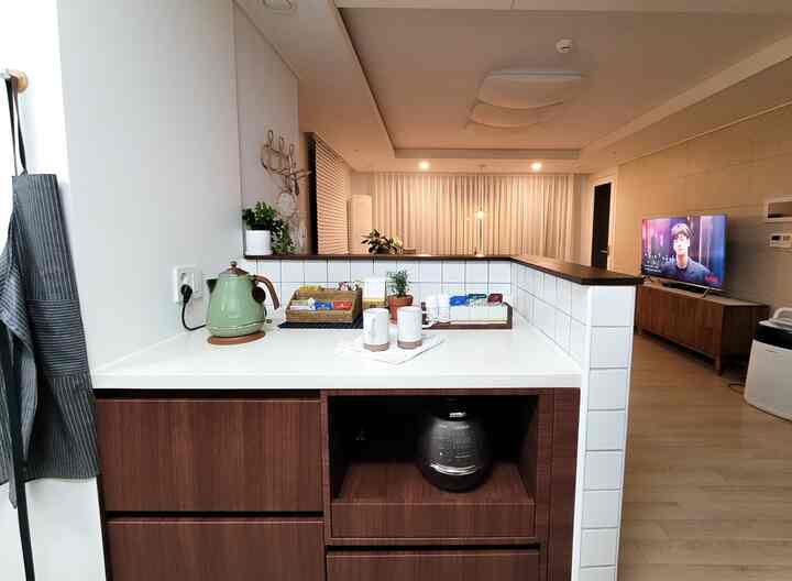 白と茶色を基調としたキッチンアイランドのあるキッチン空間、電気ケトルとマグカップが配置された清潔感のあるモダンなインテリア