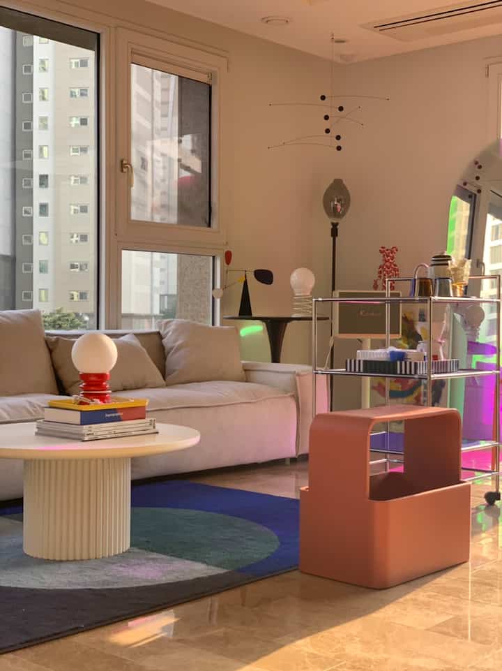 Bright beige and white toned living room featuring a round coffee table, blue rug, and pink stool with a warm modern vibe