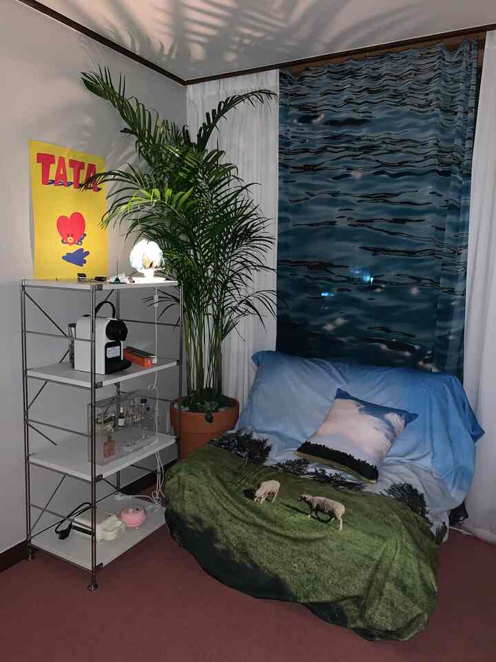 青と緑のトーンが特徴のコンパクトなワークスペース、自然柄のソファカバーとファブリックポスターが配置された居心地の良い空間