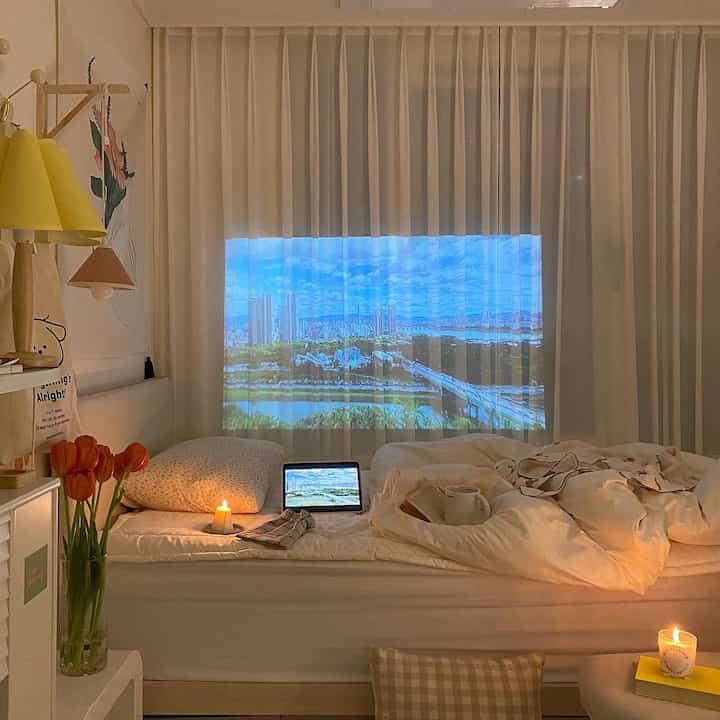 White and beige toned studio bedroom with cityscape projected on curtains and cozy mood lighting